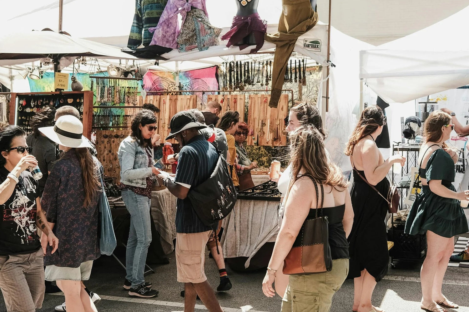 People shopping at an outdoor market with stalls and mannequins displaying clothing.